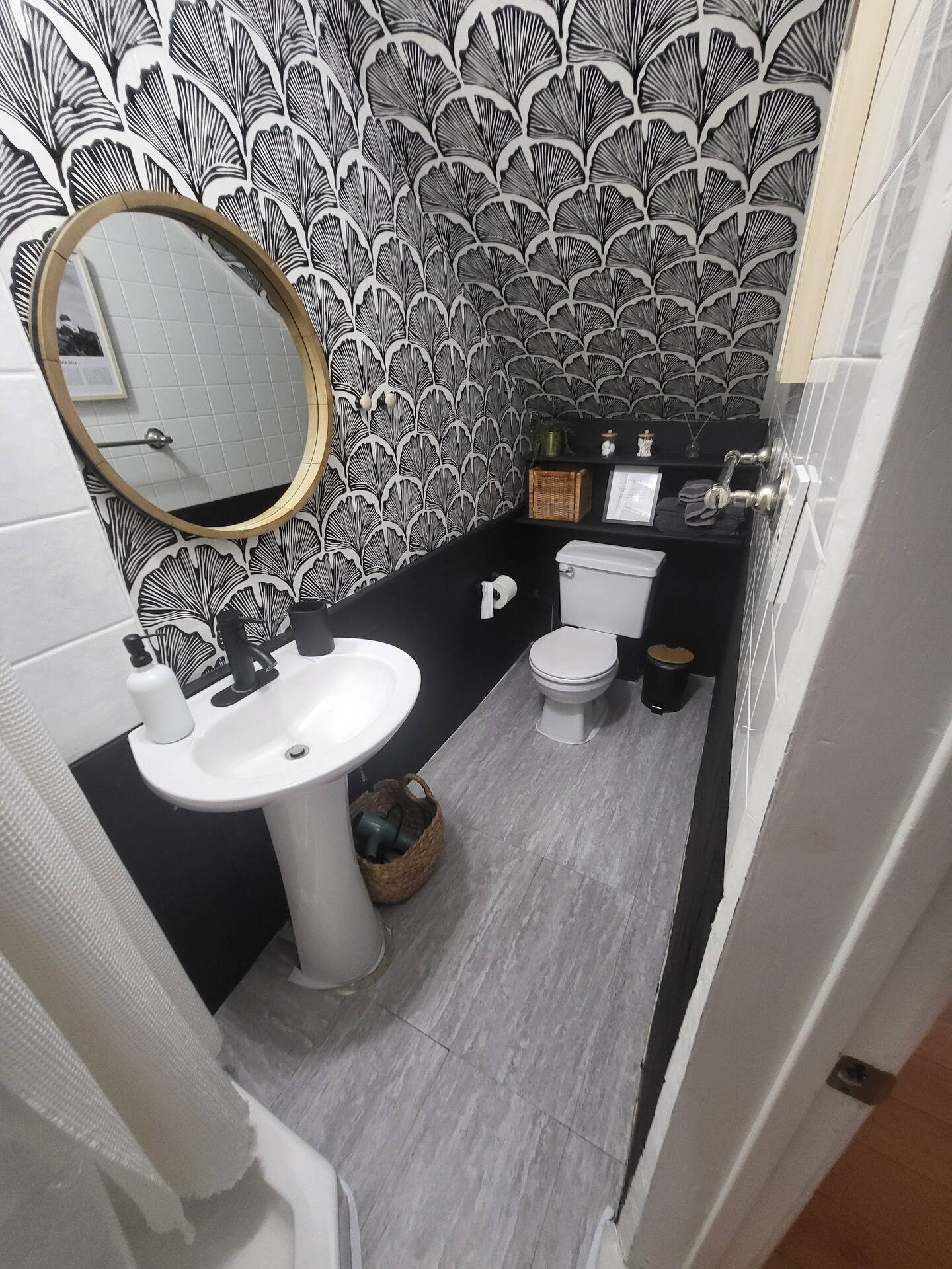 Bathroom with black and white fan-print wallpaper and brass round mirror
