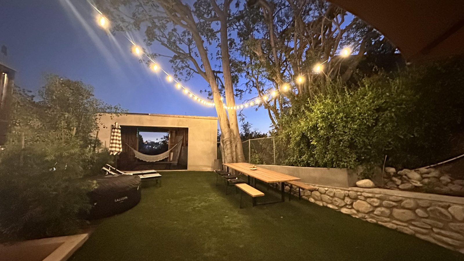 The backyard at night, string lights over the lawn and the terraced stone walls