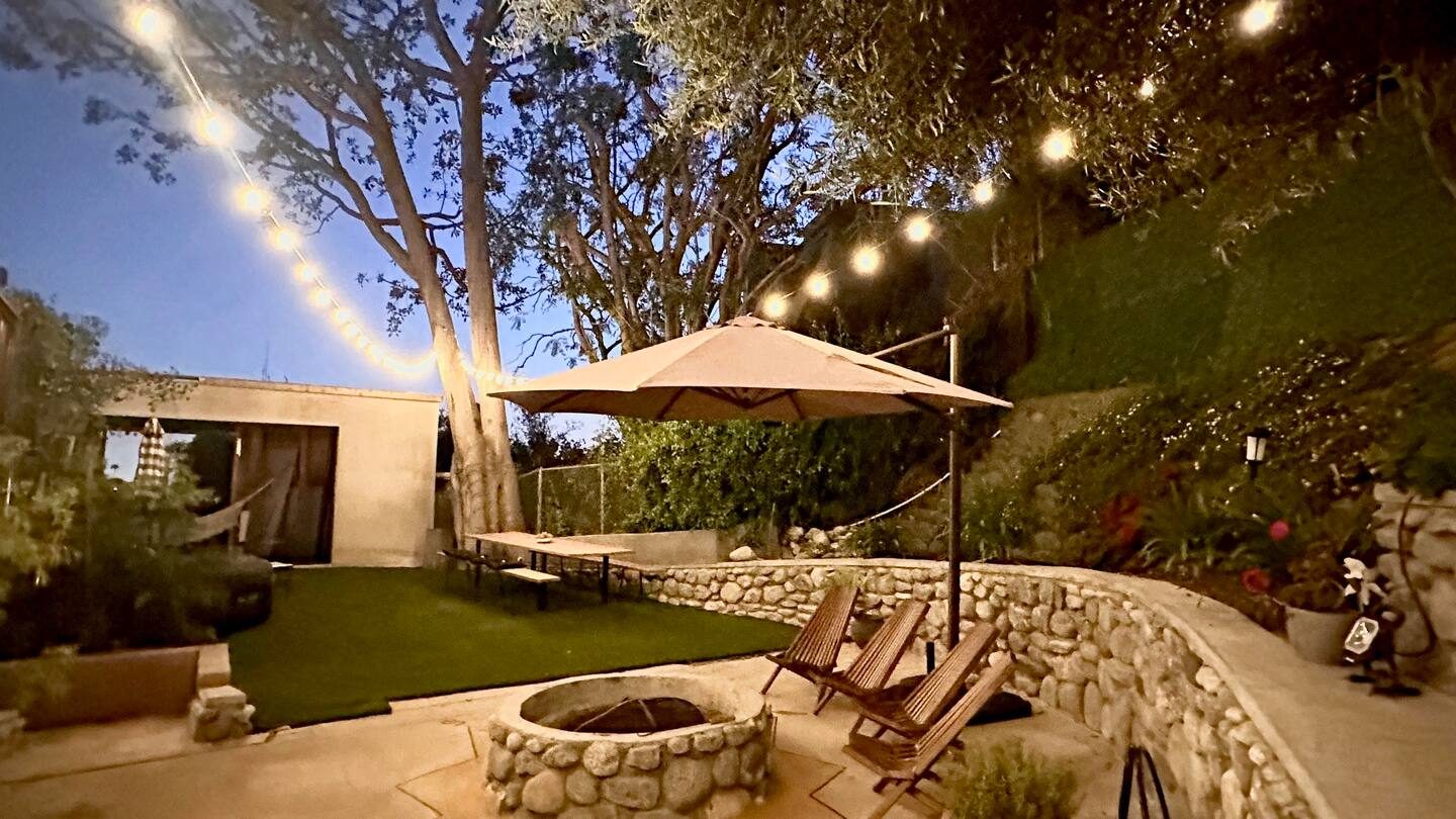 The terraced backyard at dusk, string lights over the lawn and the stone fire pit