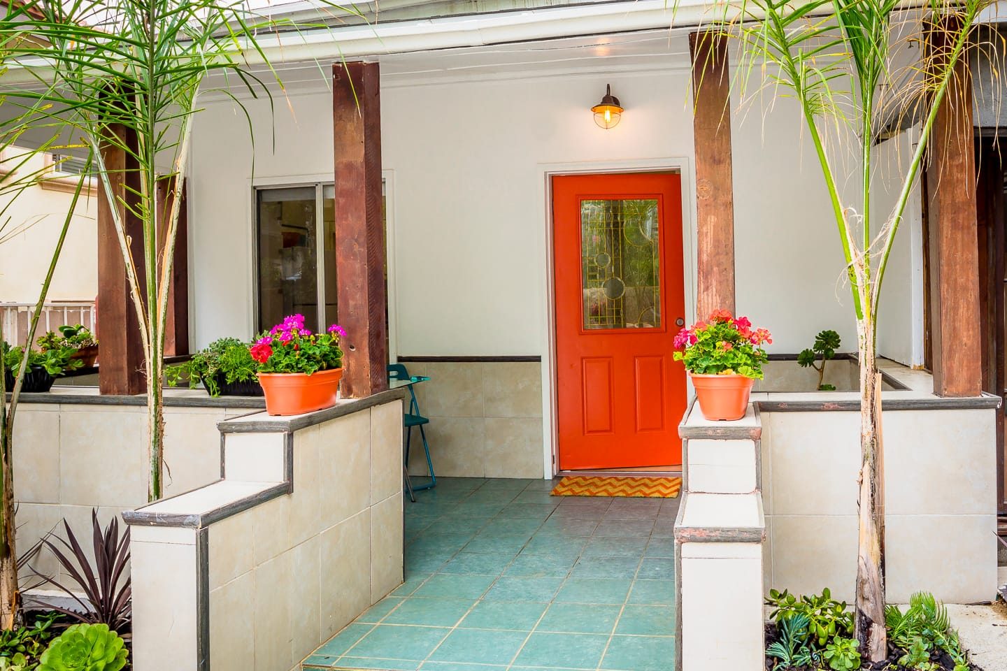 The red front door and covered porch with teal tile floor and potted geraniums